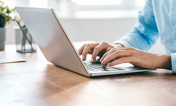 hands typing on a laptop keyboard on a wooden desk with a plant in the background workspace productivity tools two