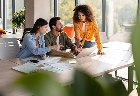 three colleagues collaborating at a table with laptop and documents in a bright office environment