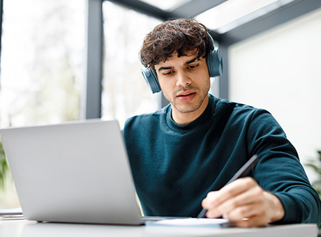 young man studying with laptop and headphones taking notes for effective learning and productivity techniques 5 essential tips