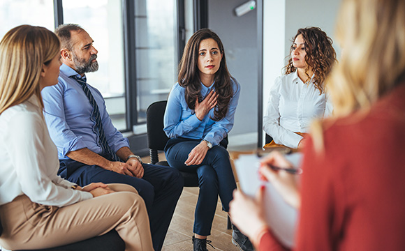 group therapy session with five people discussing emotions and personal experiences including two women and two men sitting while one woman is speaking and expressing feelings