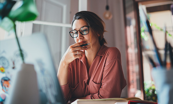 woman in glasses thinking while working on a laptop in a cozy environment focused on digital tasks and productivity 3 tips for success