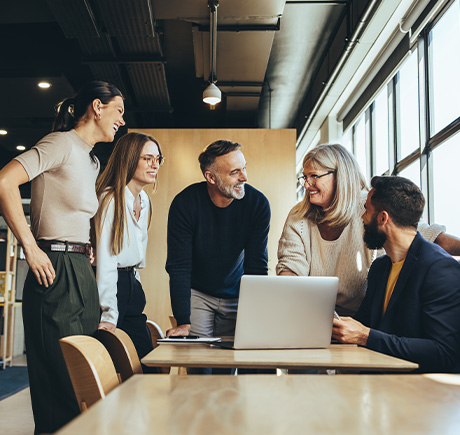 group of professionals in a modern office smiling and discussing around a laptop teamwork collaboration ideas 6 strategies