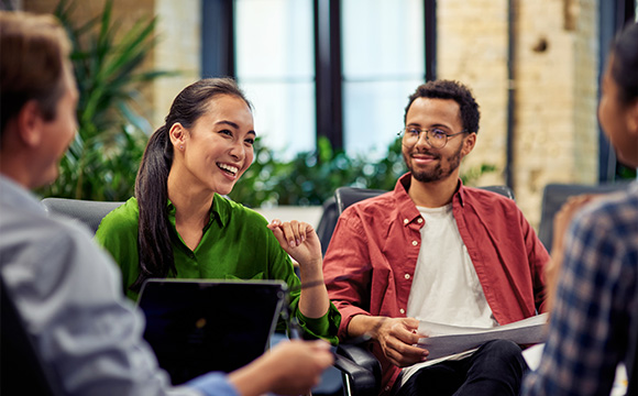 group of four people in a casual meeting discussing ideas with smiles and engagement in a bright office setting collaborating on two projects