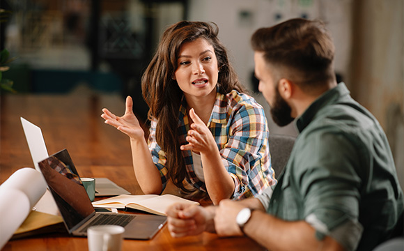 woman discussing with man in casual office setting showing collaboration ideas on two laptops and notebook