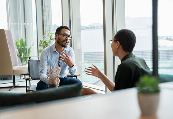 two people engaging in conversation in a modern office setting with plants and natural light discussing ideas related to communication and connection three strategies for effective dialogue
