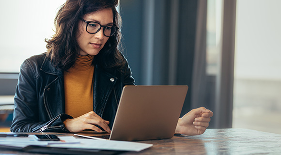 woman working on laptop at modern desk with documents and notebooks in creative workspace